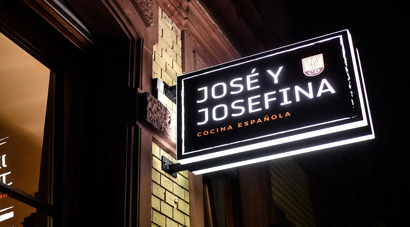 Beleuchtetes Schild „José y Josefina – Cocina Española“ an der Hausfassade bei Nacht